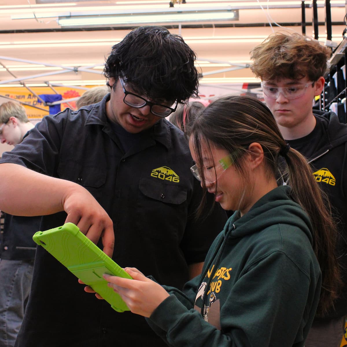 Students from different robotics team looking together at green scouting tablet.